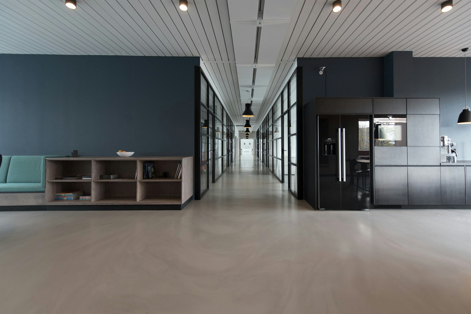 A long glazed studio interior with a full-height shelving wall and a communal table